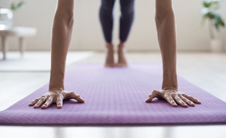 Person in der Plank-Position auf einer lila Yogamatte, mit Fokus auf Hände und Arme - perfekt für den Kraftaufbau in Ihrer Pilates Tirol Praxis.