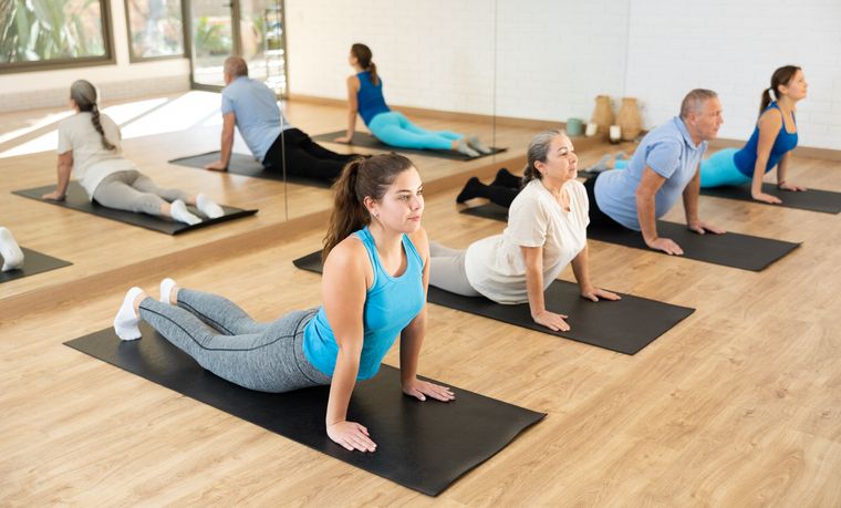 Eine Gruppe von Yogaübenden, die die Kobra-Pose auf Matten in einem hellen Pilates-Tirol-Studio mit Holzboden einnehmen.