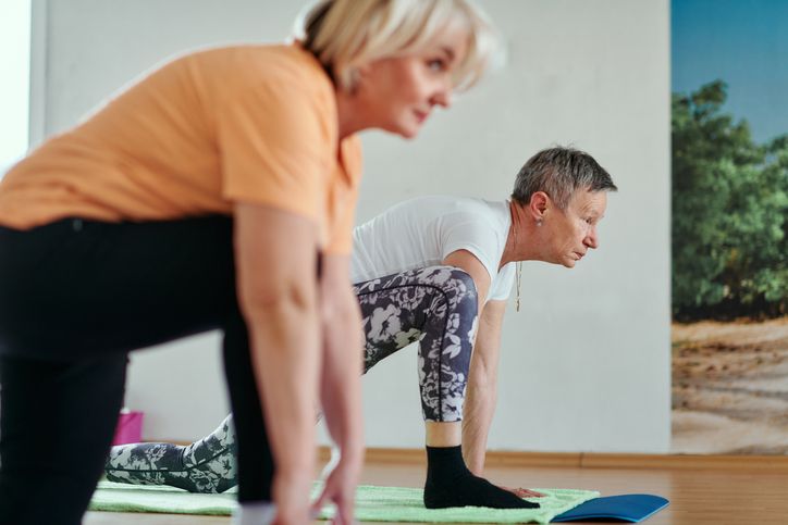 Zwei ältere Frauen dehnen sich auf Yogamatten in einem Raum, konzentrieren sich auf ihre Übungen in Sportkleidung und genießen gemeinsam eine entspannende Pilates Tirol-Sitzung.